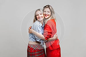 Best friends hugging. Portrait of two charming women in stylish casual clothes, isolated on gray background