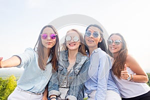 Best friends take selfies while walking in the Park. Four beautiful women wearing sunglasses are having a good day