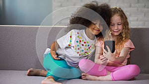 Best multiracial friends having fun on sofa and taking selfie on smartphone