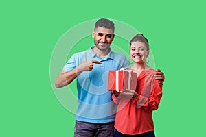 Best present for her. Portrait of happy couple in casual wear with gift box. isolated on green background