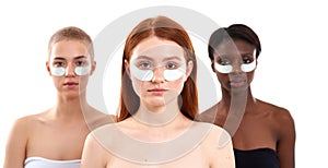 The best under eye masks. Portrait of three gorgeous multicultural young women using eye patches and looking at camera