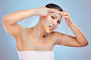 Is this the best way to get rid of it. Studio portrait of an attractive young woman squeezing a zit on her face against photo