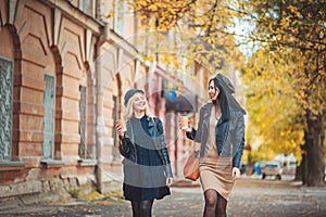Best weather ever! Outdoors shot of young women with coffee on city street. Two fashion girls walking outdoor with cofee.