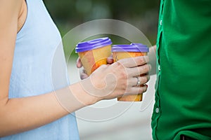 Betrothed couple with coffee cups in hands, walking in park.