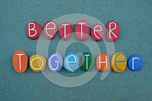 Better together, motivational slogan text composed with multi colored stone letters over green sand