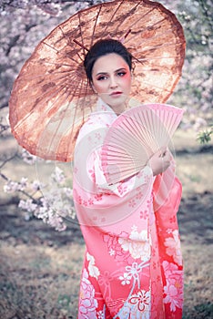 Beuatiful girl with japanese traditional kimono and umbrella in orchard during spring