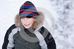 Beuatiful happy boy wearing winter clothes standing against snow background