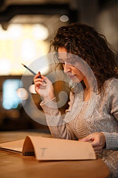 Beutiful brunette business woman make notes in her notepad in cozy restraunt. dressed in gray knitted sweather