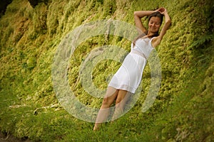 Beutiful young girl leaning against green moss wall near road. Expression of relaxation and happiness on face