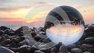 Beutifull sunset reflection inside crystal ball on stones, sun over water, beach, landscape