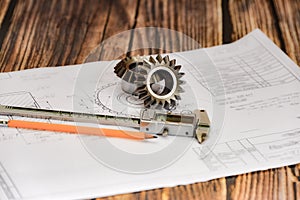 Bevel gear, vernier caliper and pencil on a technical drawing, concept of design and engineering production