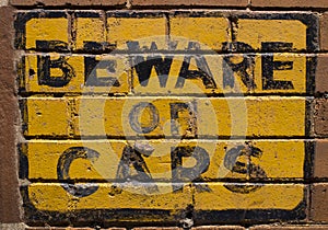 Beware of Cars sign on a brick wall