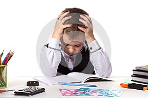Bewildered pupil sitting with lowered eyes at the desk with hands over the head surrounded with stationery