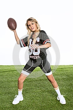 bewildered young woman in american football uniform throwing ball while standing on green grass