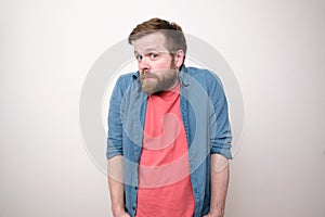 Bewilderment bearded man in casual clothes looks thoughtfully and in surprise, thrusting hands into pockets and lifting