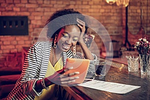 Bewitching Afro-American woman watching funny video on tablet at bar