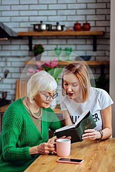 Bewitching dame sitting at table and reading Bible with lady