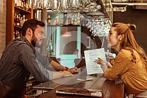Bewitching woman discussing a menu with handsome dark-haired bearded bartender