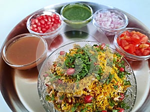 Bhel chaat in a plate with onion,tomato, pomegranate, tamarind water and mint water as a background