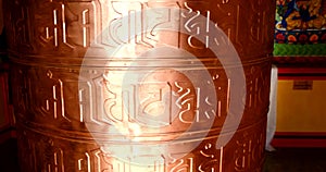 Bhuddhist prayer wheel golden inscribed with a sanskrit prayer and creamy bokeh .