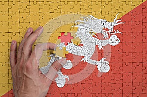 Bhutan flag is depicted on a puzzle, which the man`s hand completes to fold