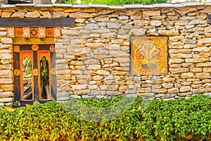 Bhutanese stone boundary wall with colorful carving wood artwork, green bush and copy space for your text. Bhutan style house deco