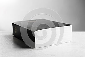 Bible with black cover on light gray table, closeup. Christian religious book