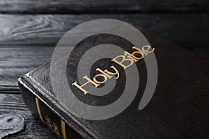 Bible with dark cover on black wooden table, closeup. Christian religious book