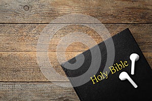 Bible and earphones on wooden background, top view. Religious audiobook