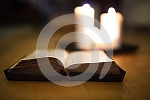 Bible laid on wooden floor, burning candles in the background