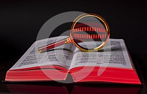 Bible or law code book with magnifying glass for analysis over black background