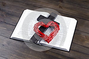 Holy Bible open. Cross, crucifixion of Jesus. Red heart. Love Agape concept. On a wooden table.