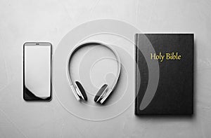 Bible, phone and headphones on grey background, flat lay. Religious audiobook