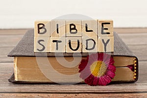 Bible study text on wood cubes, closed Holy Bible Book with golden pages, and flower on rustic table with white background