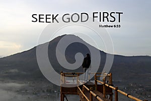 Bible verse quote - Seek God first. Matthew 6:33 With person standing on natural wooden bridge against the misty mountain. photo