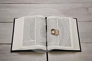 Bible with wedding rings on white wooden table