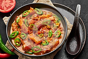 Bicol Express Stew in black bowl on dark slate table top. Filipino cuisine spicy pork belly coconut milk curry