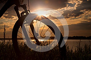 Bicycle on the background of a summer evening landscape. Silhouette of a bicycle in the grass near the lake