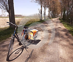 A bicycle with big panniers at a road with trees in the dutch countryside in springtime