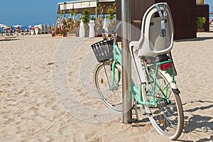 Bicycle with child chair stands on pillar on the beach on sunny day