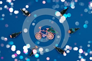 Bicycle with Christmas tree surrounded by snowed trees on classic blue with festive colorful bokeh
