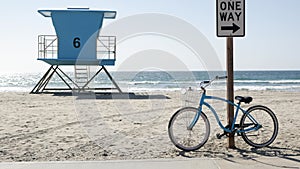 Bicycle cruiser bike by ocean beach, California coast USA. Summer cycle, lifeguard tower, road sign