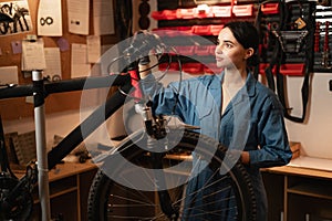 Bicycle female mechanic repairing bicycle doing his professional work in workshop or garage.