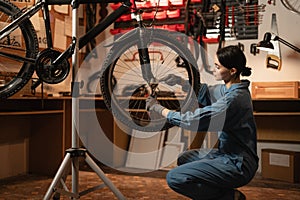 Bicycle female mechanic squatting repairing bike doing his professional work in workshop or garage.