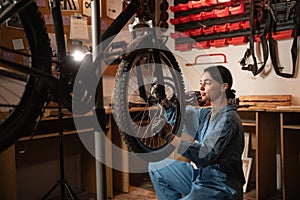 Bicycle female mechanic squatting repairing bike doing his professional work in workshop or garage.
