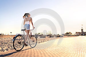 Bicycle fun on beach promenade. Happy woman riding bike on sunny summer boulevard. Seaside waterfront street for cycling.