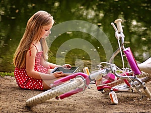 Bicycle girl recreation and watch tablet pc sits near water.