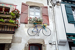 Bicycle is hanging under the window with wooden shutters on the wall of the facade of the building. Traditional red and white