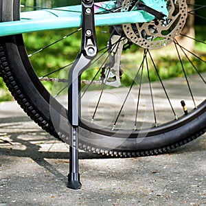 Bicycle kickstand with rear bicycle wheel standing on the asphalt with green grass on the background