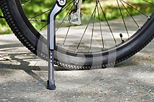 Bicycle kickstand with rear bicycle wheel standing on the asphalt with green grass on the background